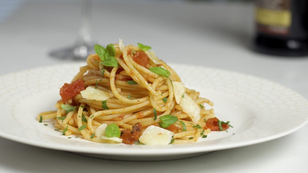 Spaghetti and Tomato Sauce with large pieces of grated Parmesan Cheese on a white plate.  