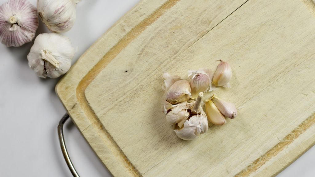 Fresh Head of Garlic half crushed on cutting board.